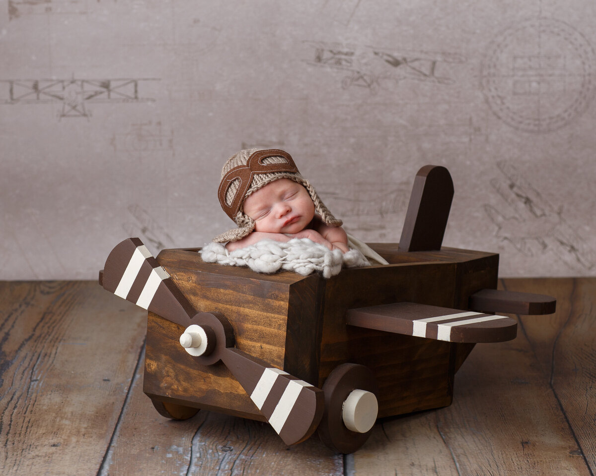 Newborn baby photographed in a little wooden plane in the  studio at Life in Pink Photography