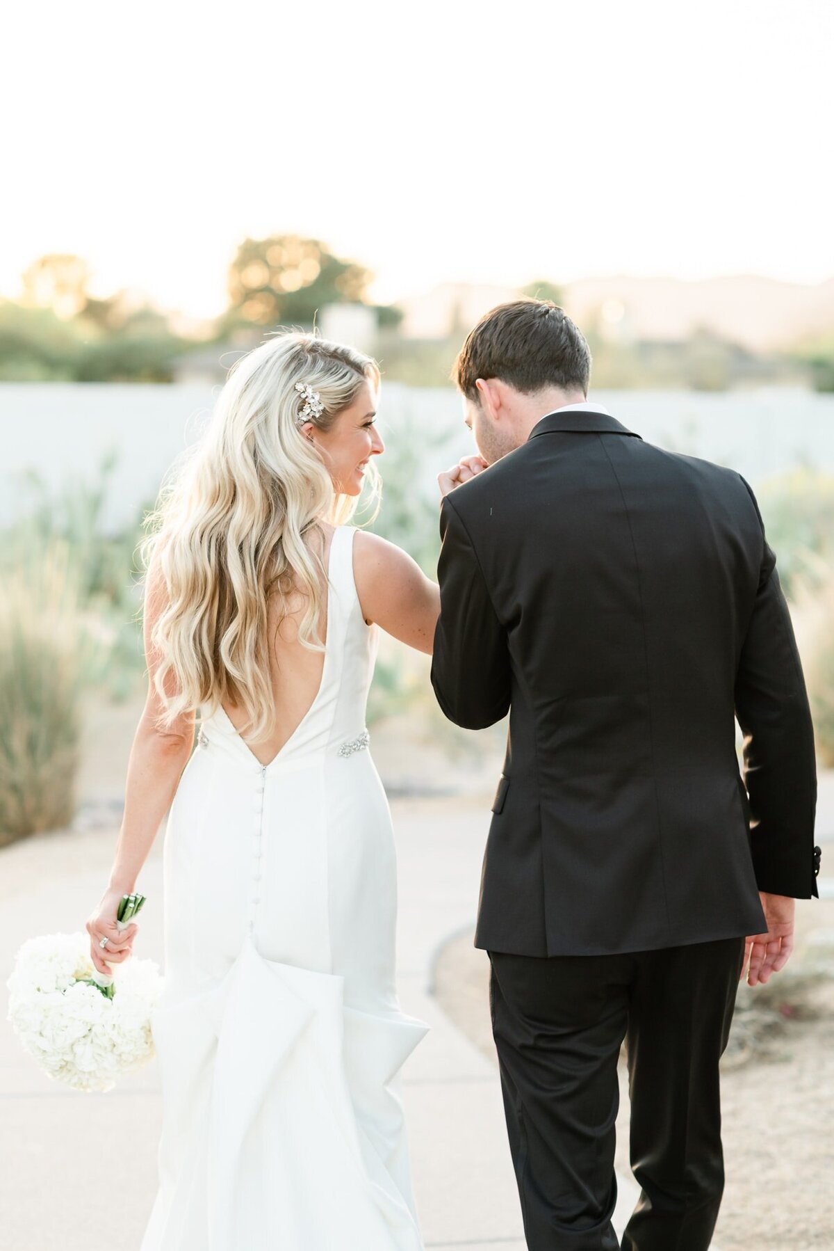 Groom kisses brides hand as the walk down path at Andaz Resort Scottsdale