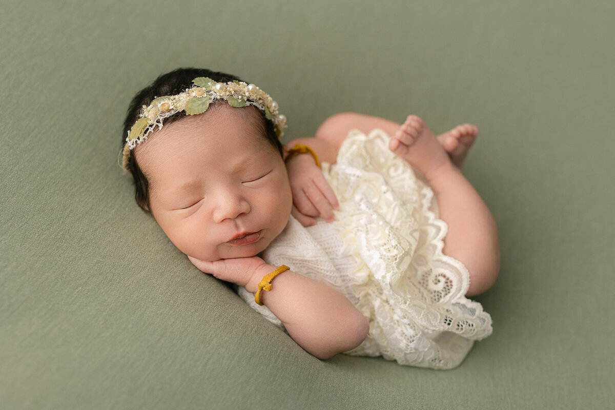 haldimand county n ewborn photographer captures adorable photo of baby girl laying on green backdrop with frilly dress on