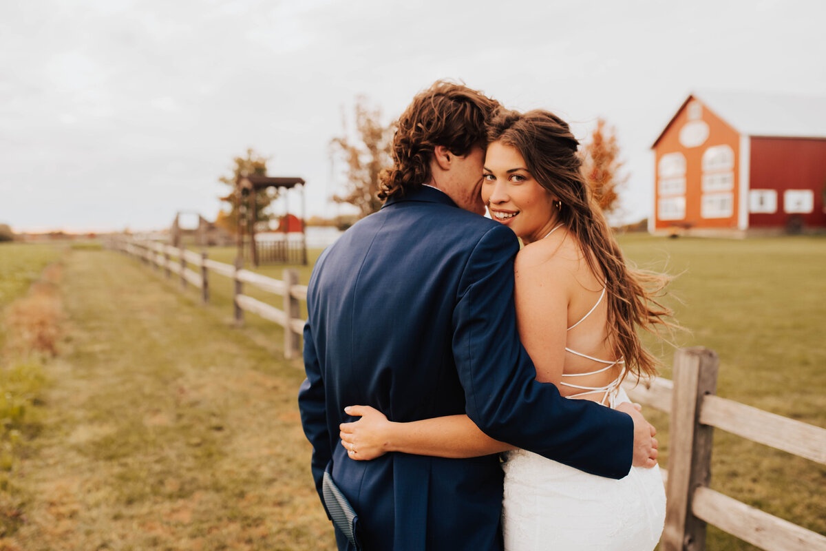 bride and groom posing while walking in front of a red barn at their Michigan barn wedding