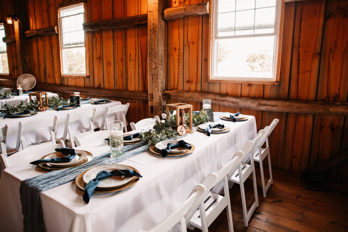Details of a wedding reception table with white linen, chairs and candles with a blue runner and napkins