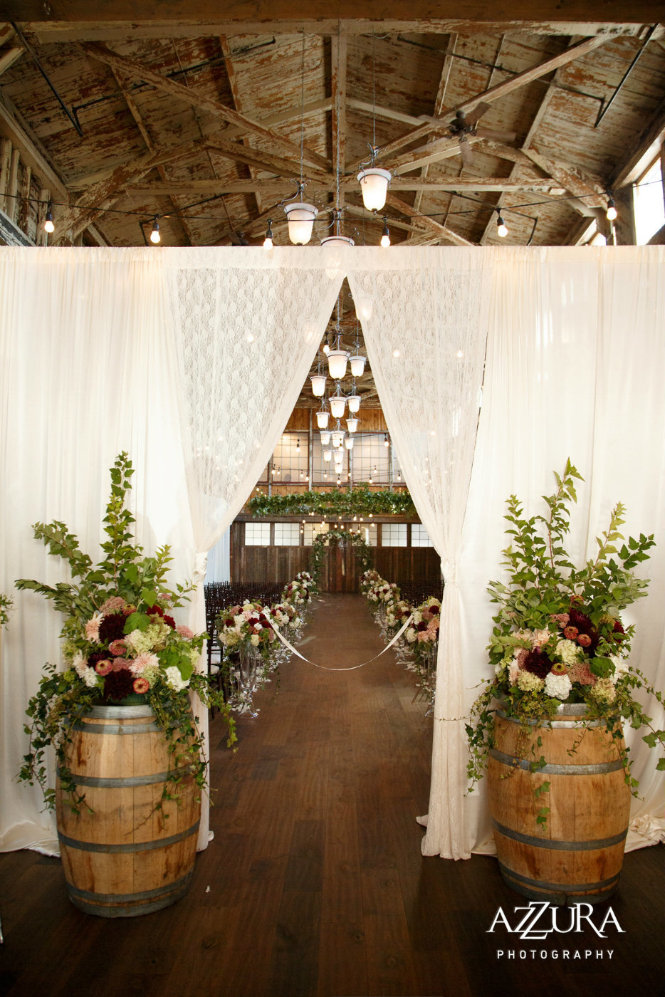 Sodo Park wedding ceremony entry decor with draping, barrels with large flower arrangements and welcome sign decorated in greenery vines