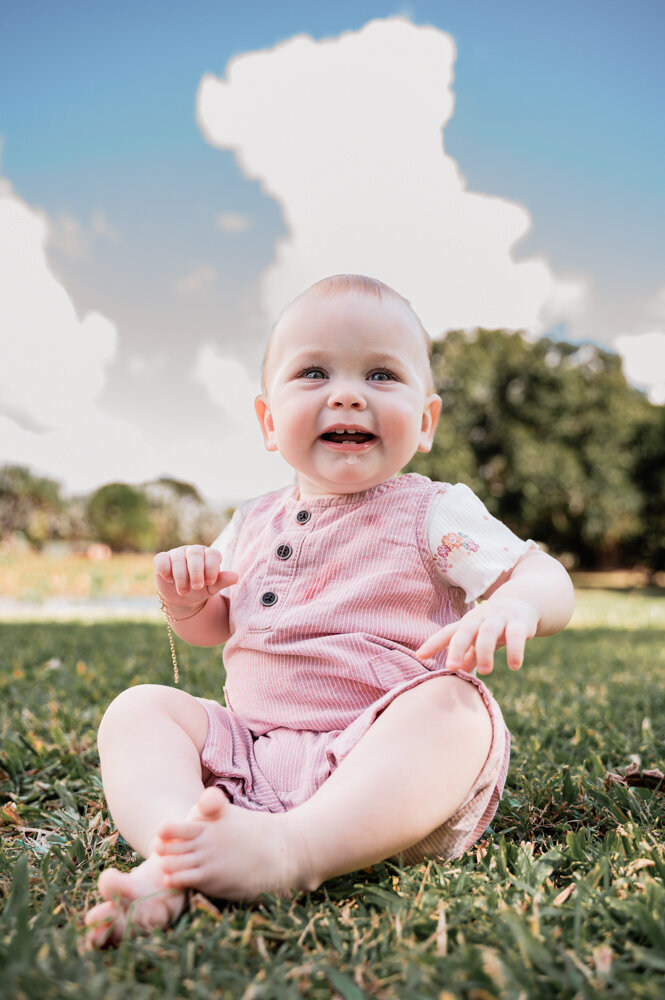 baby girl sitting in a garden smiling at the camera - Townsville Child Milestone Photography by Jamie Simmons
