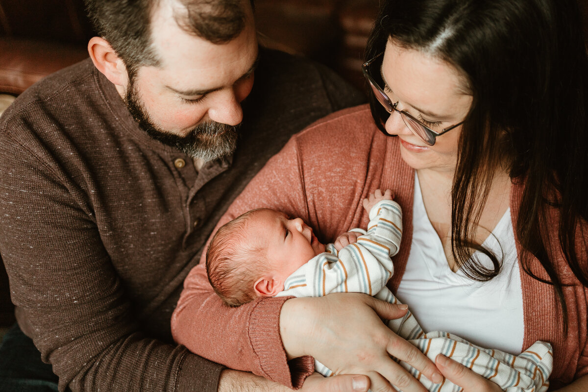 New mom and dad looking down lovingly at newborn baby boy in striped outfit in Longmont Colorado
