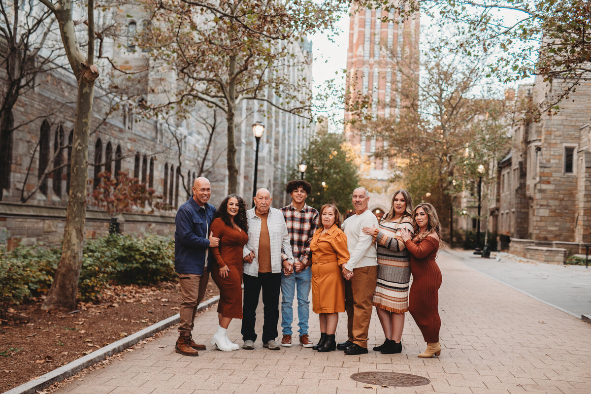A large, multigenerational family poses together on a scenic Yale University campus walkway during a fall family photography session in Connecticut. Captured by Nicole Mele Photography, highlighting love, connection, and togetherness.