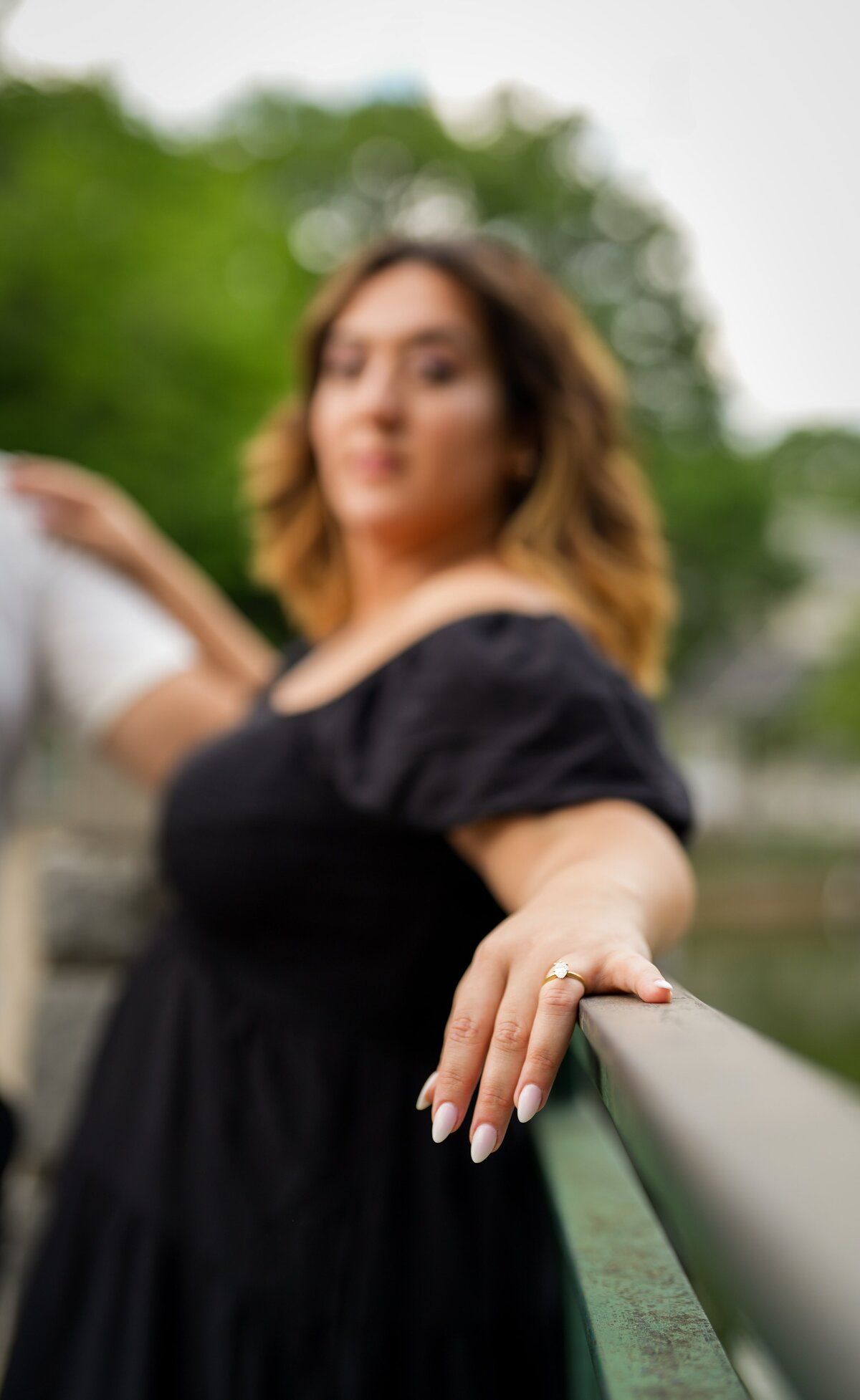 Close-up of a woman’s hand resting on a railing, showing an engagement ring with a blurred background