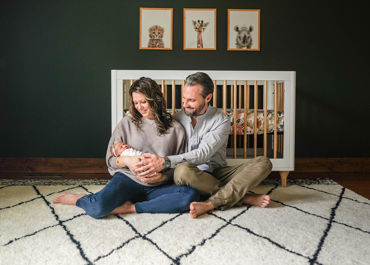 A mom and dad hold their newborn baby girl in front of her crib