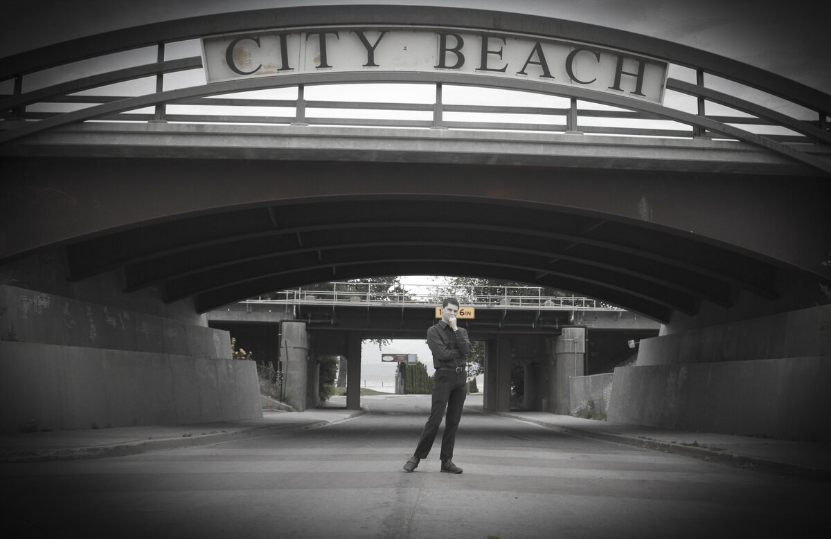 Man standing under a bridge with a sign above reading City Beach