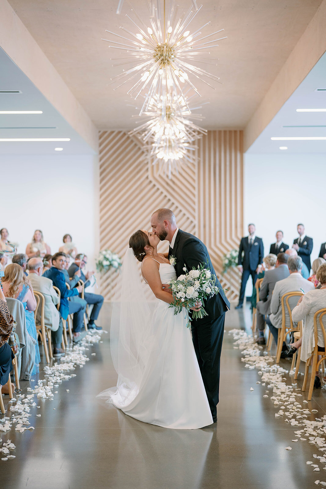 Bride and groom sharing a kiss halfway down the aisle moments after their ceremony, surrounded by clapping guests at Leona Road Wedding Venue in Grand Rapids MI.