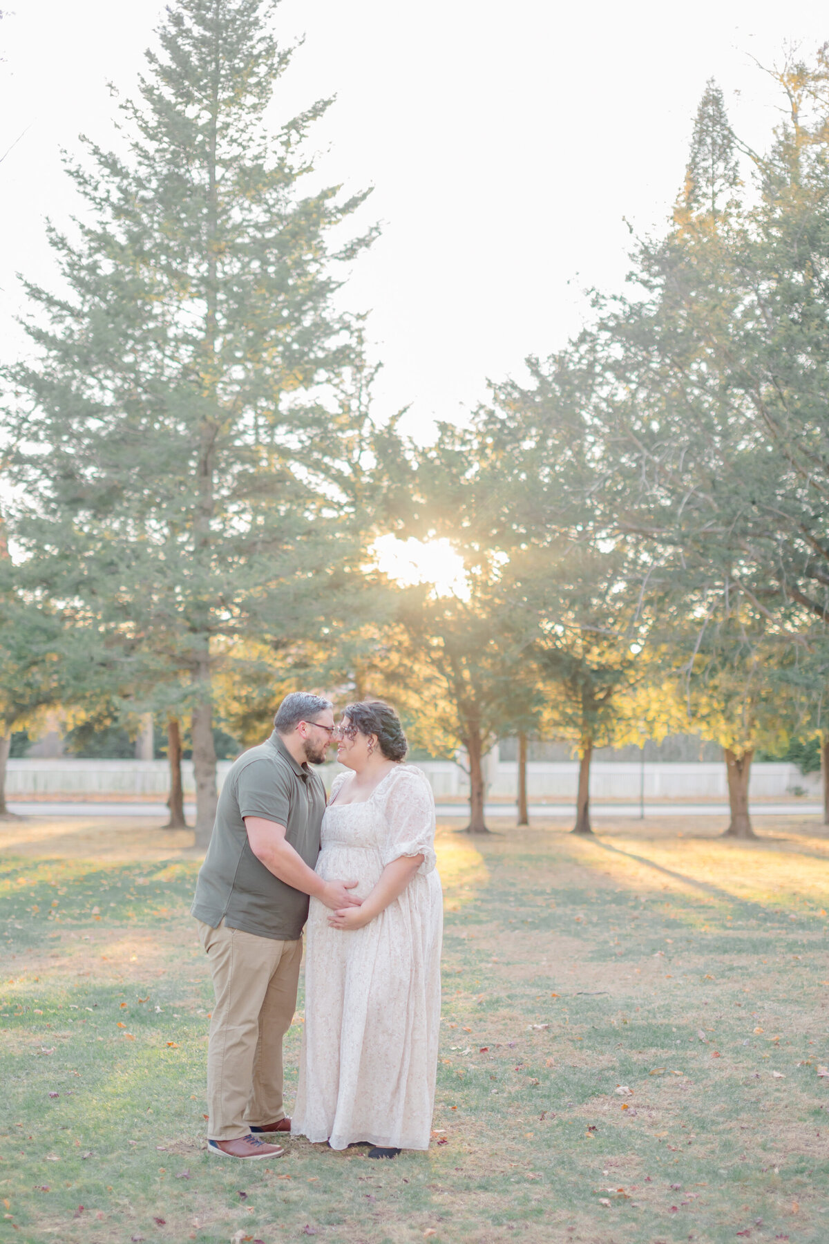 Pregnant mom with her partner in a field of tall grass, smiling at each other as they anticipate the arrival of their baby