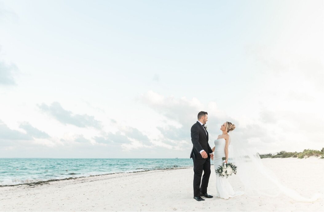 Bride and groom standing together on a white sand beach during their destination wedding