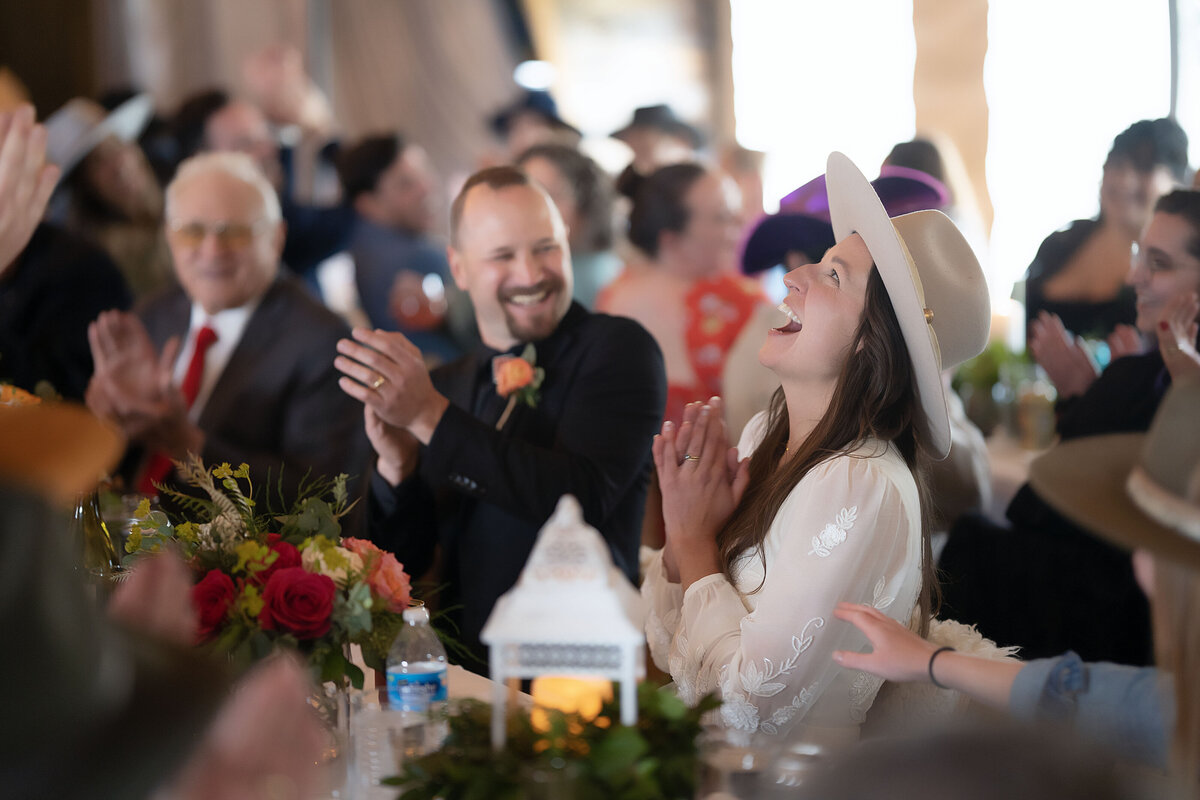 A bride claps her hand and laughs as she looks up after a joke during their speeches in their Aspen, Colorado ceremony.