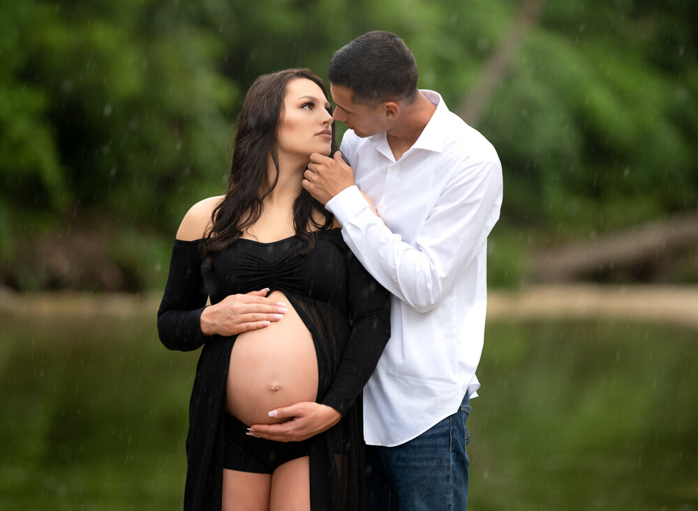 Intimate maternity session with couple in black outfits by the water surrounded by greenery in Texas