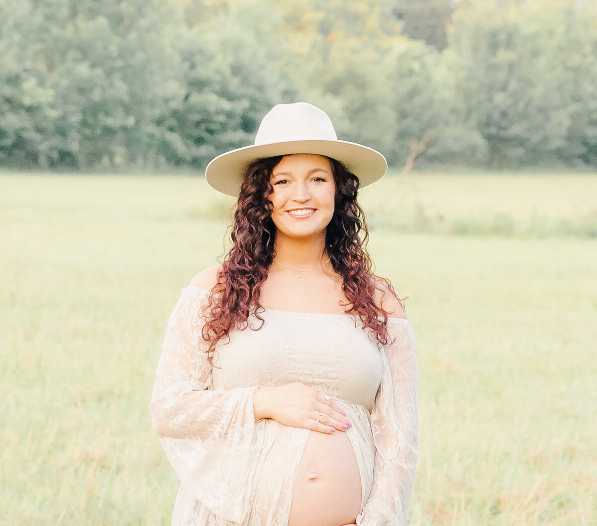 pregnant mother wearing hat showing her pregant belly in field in middle Tennessee