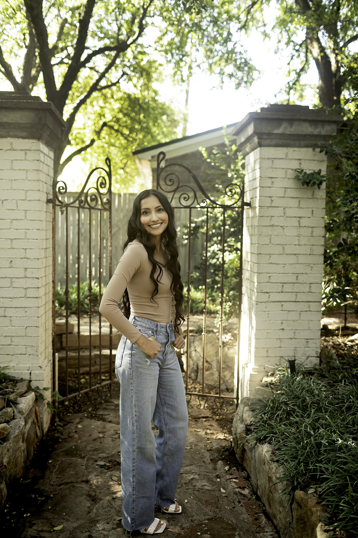 A high school senior walking along the garden paths of Chandor Gardens, surrounded by blooming flowers and lush greenery, reflecting on the next chapter of life.