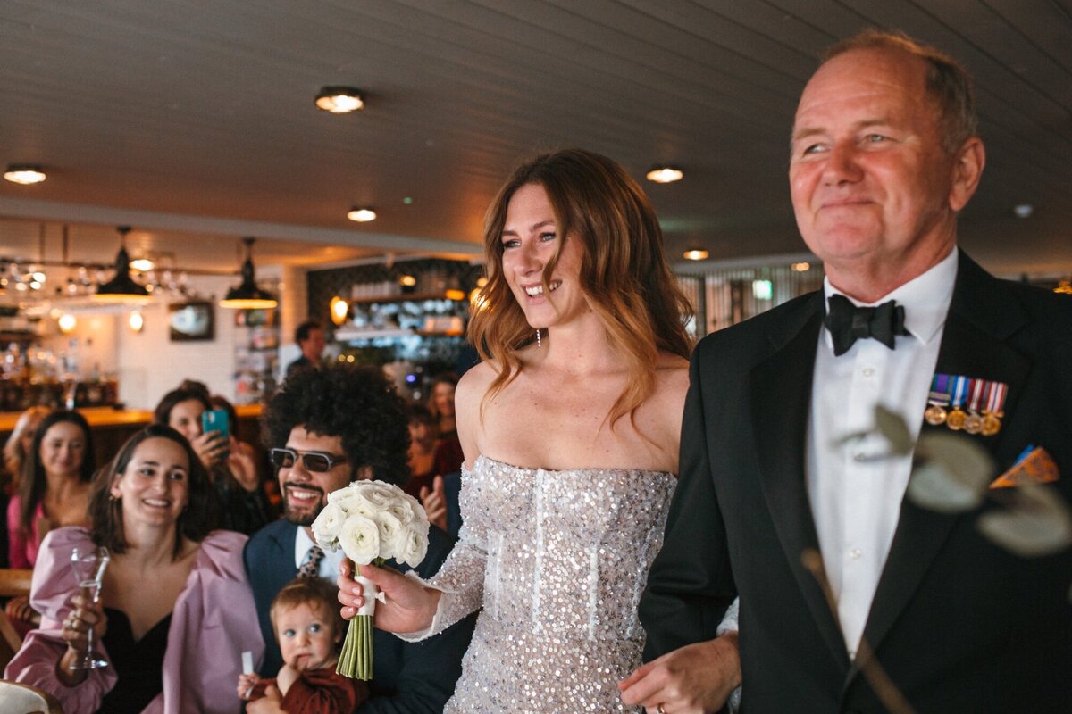 Bride and Dad approach the ceremony together smiling with joy