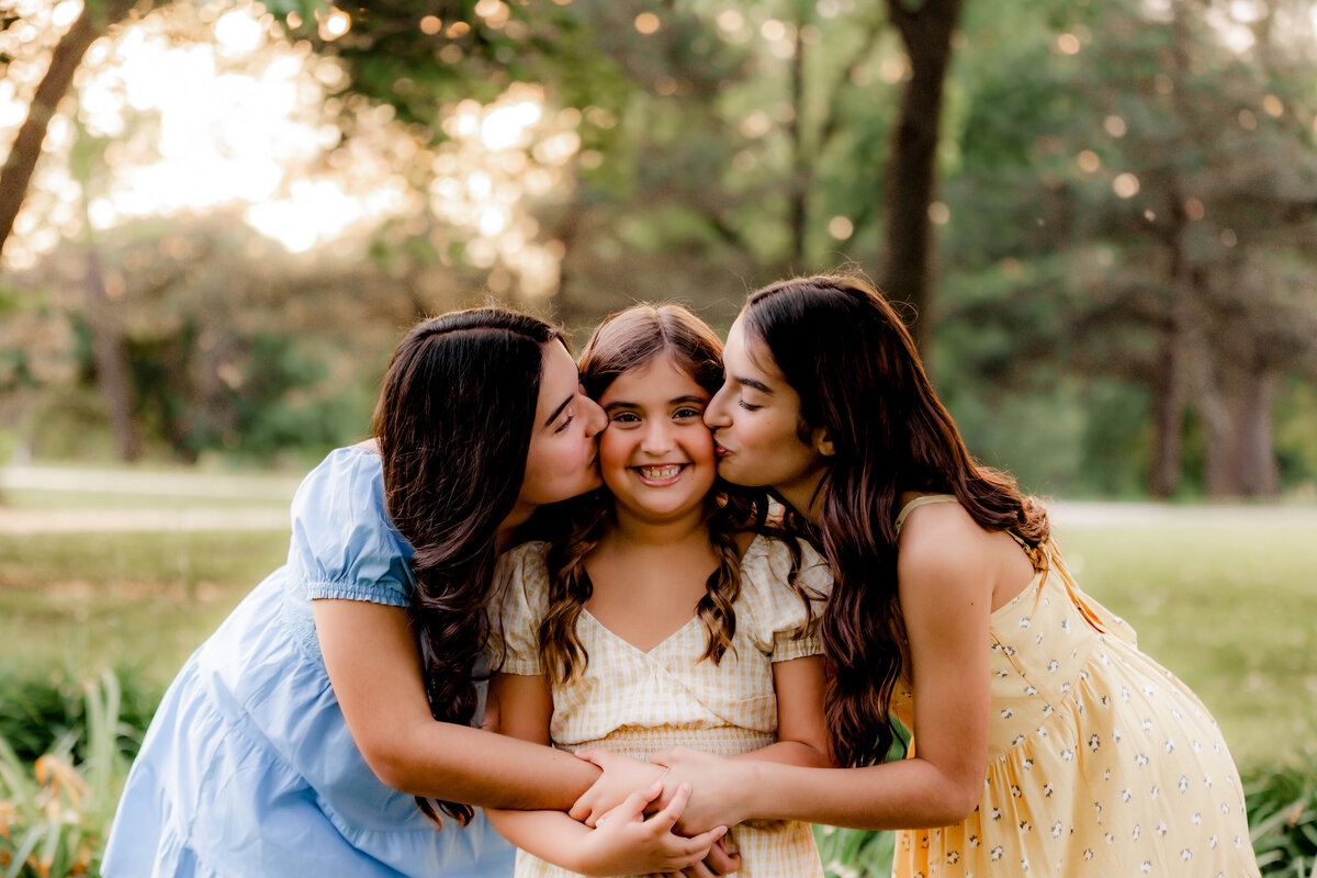 Sisters kiss their little sister on the cheek.
