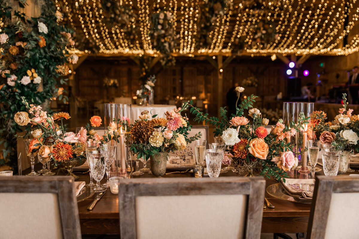 Beautiful fall floral centerpieces warm this reception space with a sunset color palette. Garden roses, ranunculus, double brownie tulips, and lisianthus create hues of terra cotta, blush pink, copper, and yellow. Designed by Rosemary and Finch in Nashville, TN.