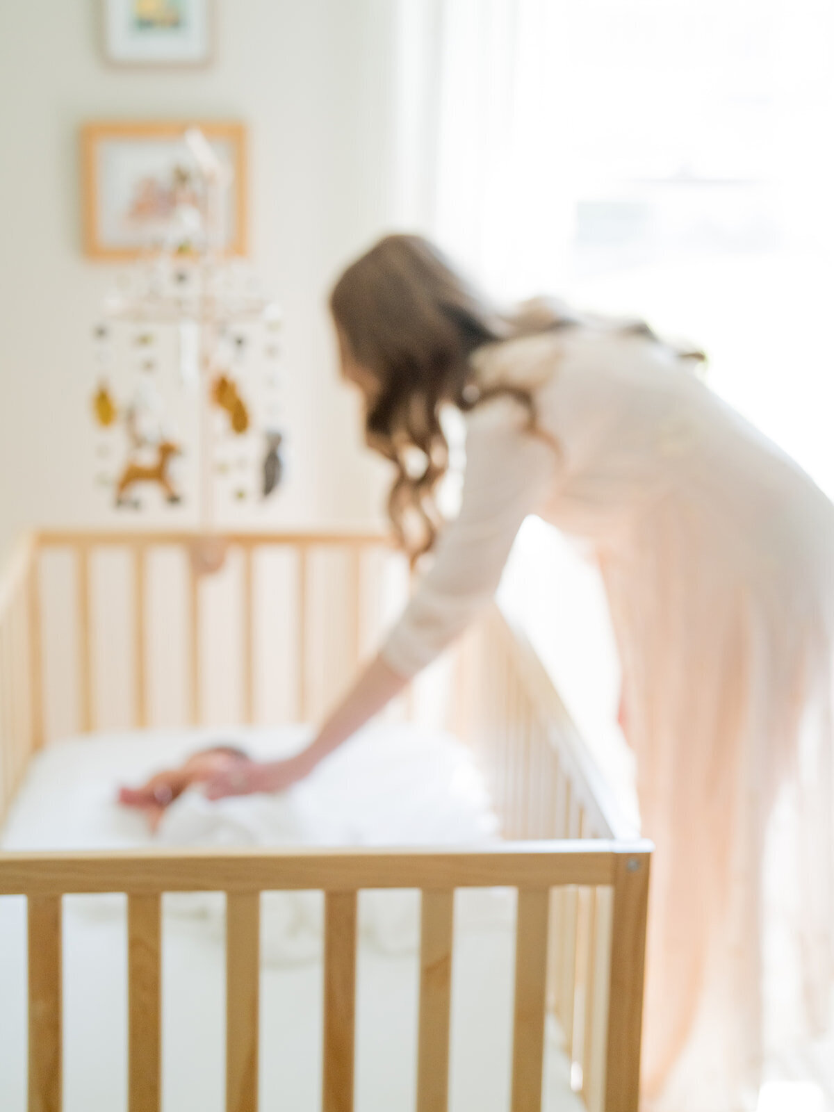 Out-of-focus mother leans down to place a hand on her baby boy in his crib during their Arnold Maryland newborn session.