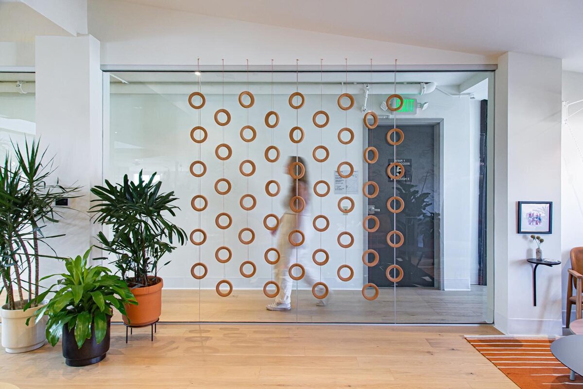 Glass wall divider with circular hanging accents, with plants and a blurred figure walking behind the glass.
