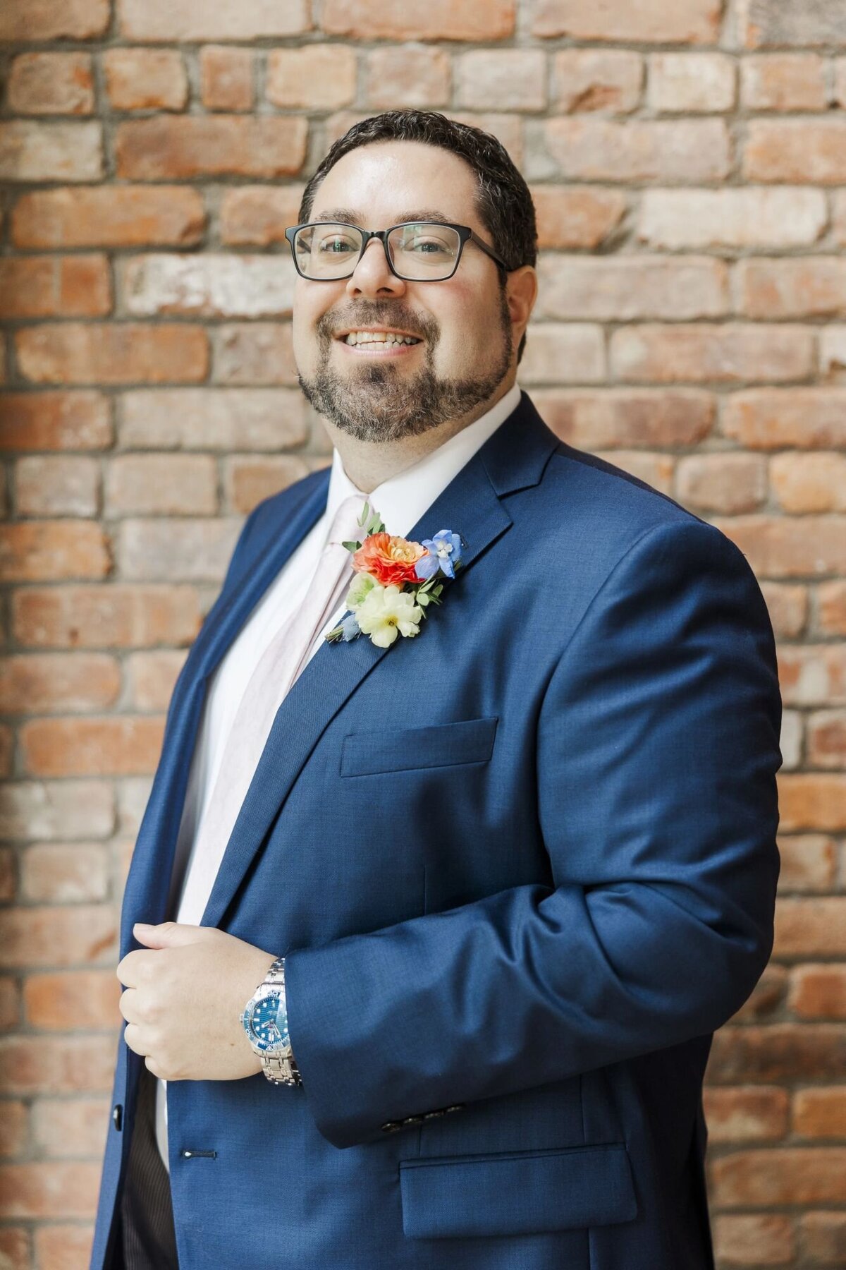Groom stands in front of a brick wall in The Roundhouse ceremony space on his wedding day