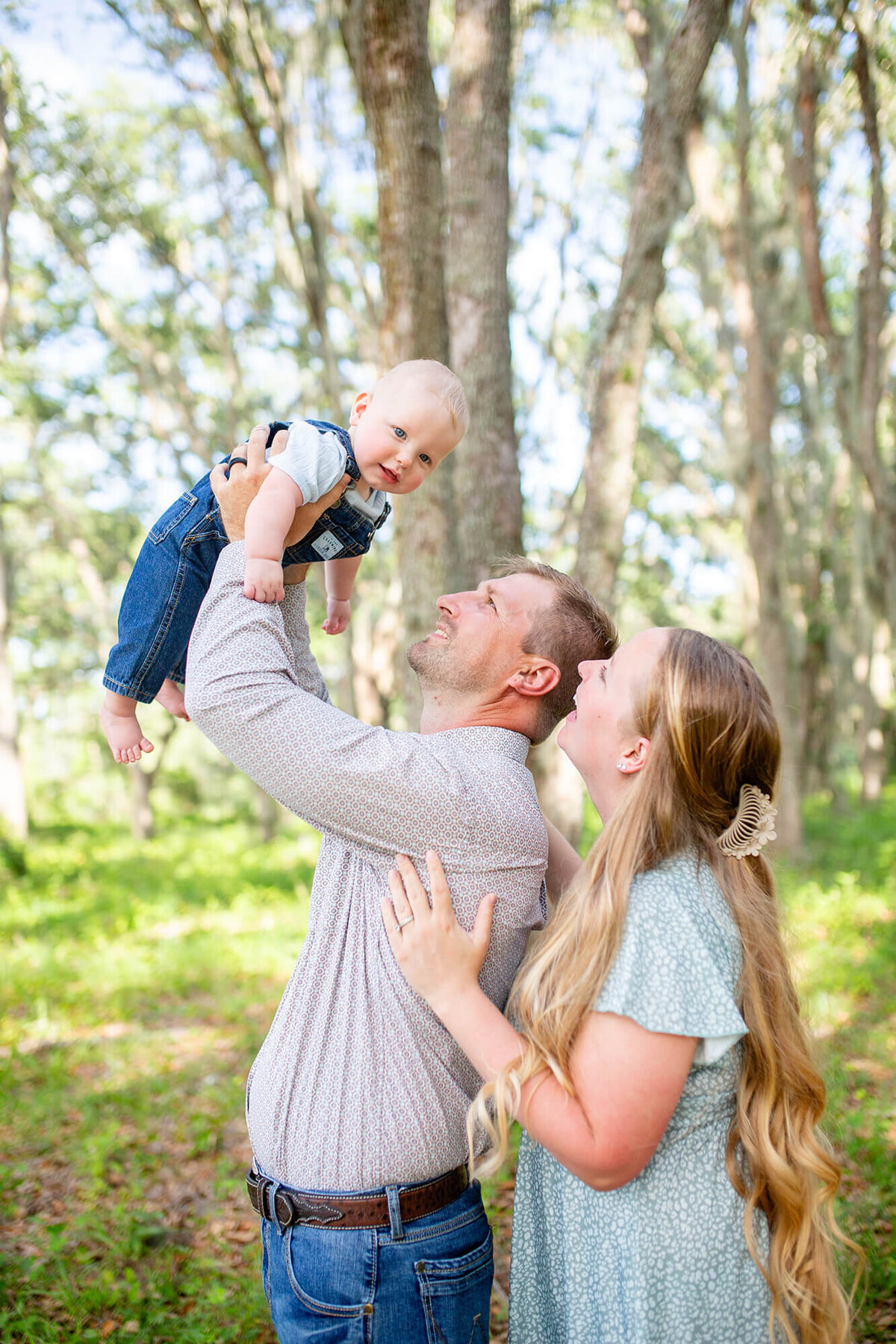 Father playing with little boy and mother looking over his shoulder at the baby boy in an intimate and playful family portrait 