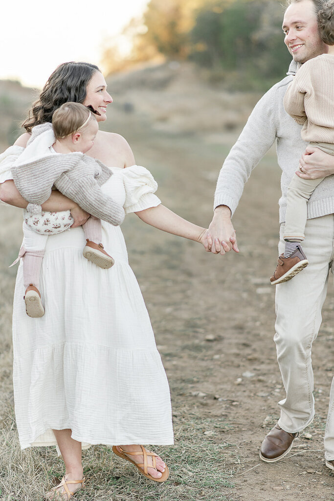 Mom and dad hold hands and walk as they carry their two children