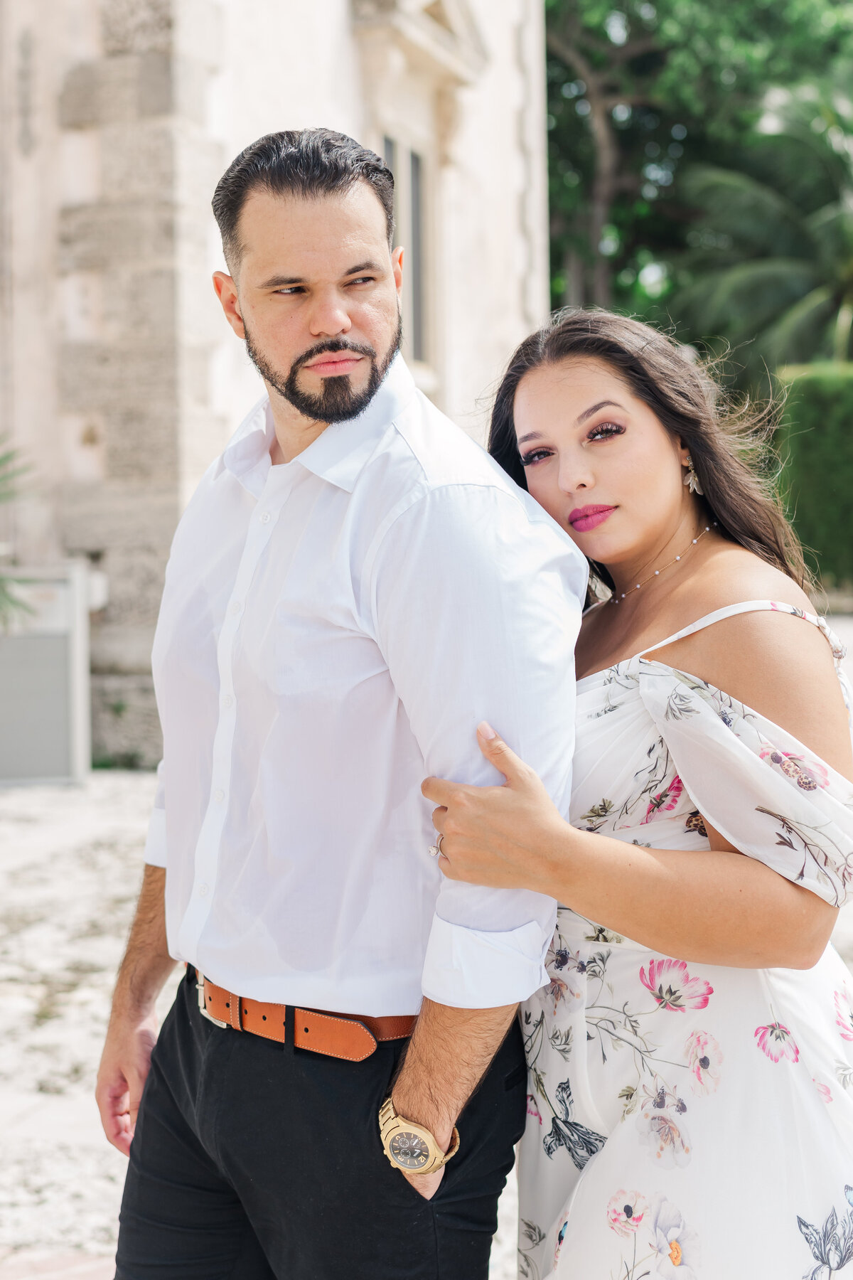 a wom with an engagement ring touching a mas's  arm while looking at the camera
