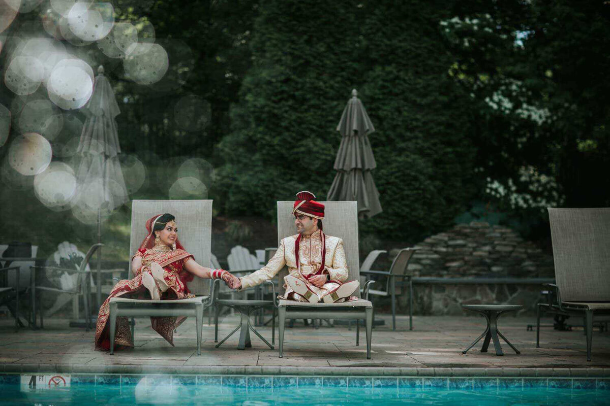 Bride and groom during portraits before thier Indian wedding ceremony at the Valley Forge Casino Resort. The bride and groom are sitting near the pool holding hands, taking some moments to unwind before their grand Indian wedding ceremony.