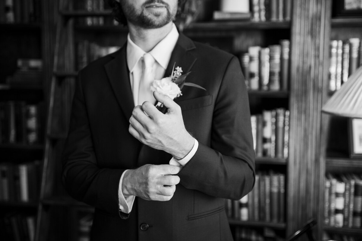 A close up shot of a groom adjusting his cufflinks in the library at The Manor House in Littleton, Colorado.