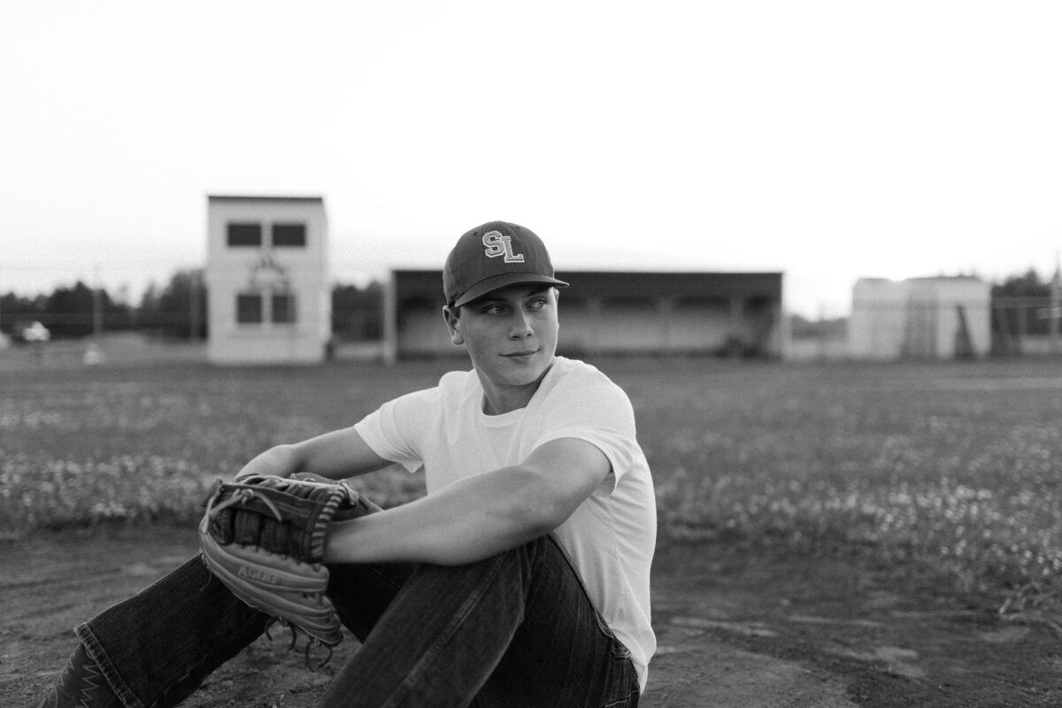 Baseball senior perches on a baseball mound on the field while confidently staring off into the distance.