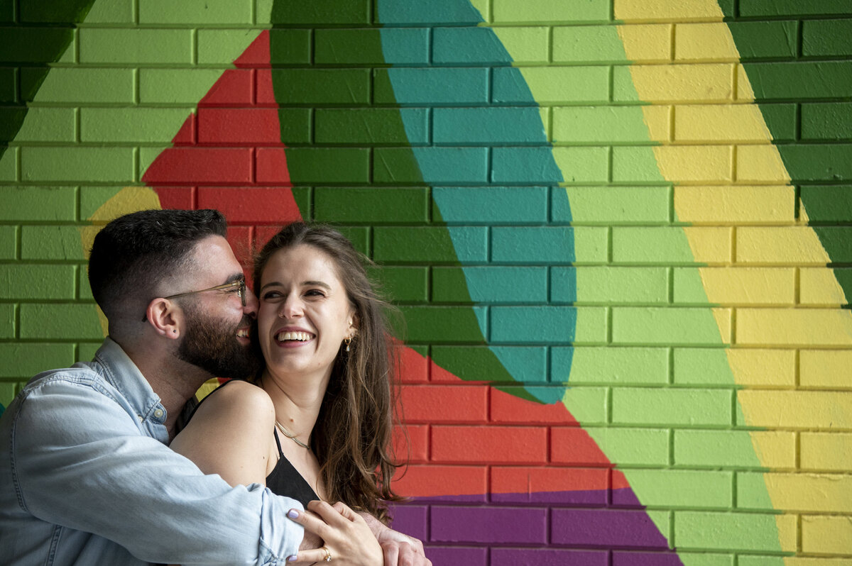 A person standing behind their partner leaning into them as they both smile 