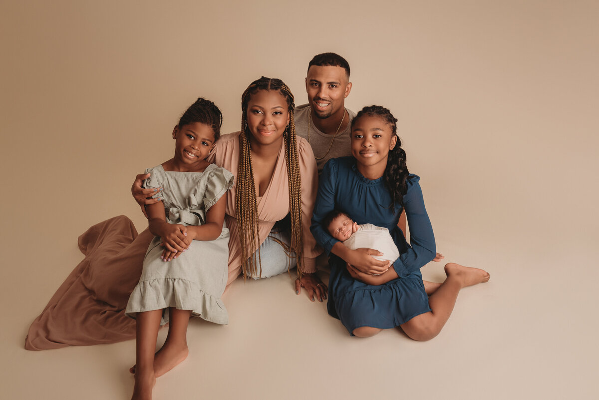 family newborn portraits at Atlanta newborn studio with baby swaddled in cream fabric and family wearing neutral dress sitting down smiling at camera