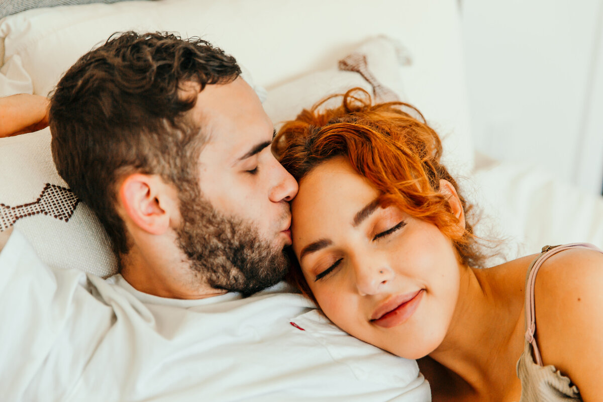 husband kissing wife while laying in bed