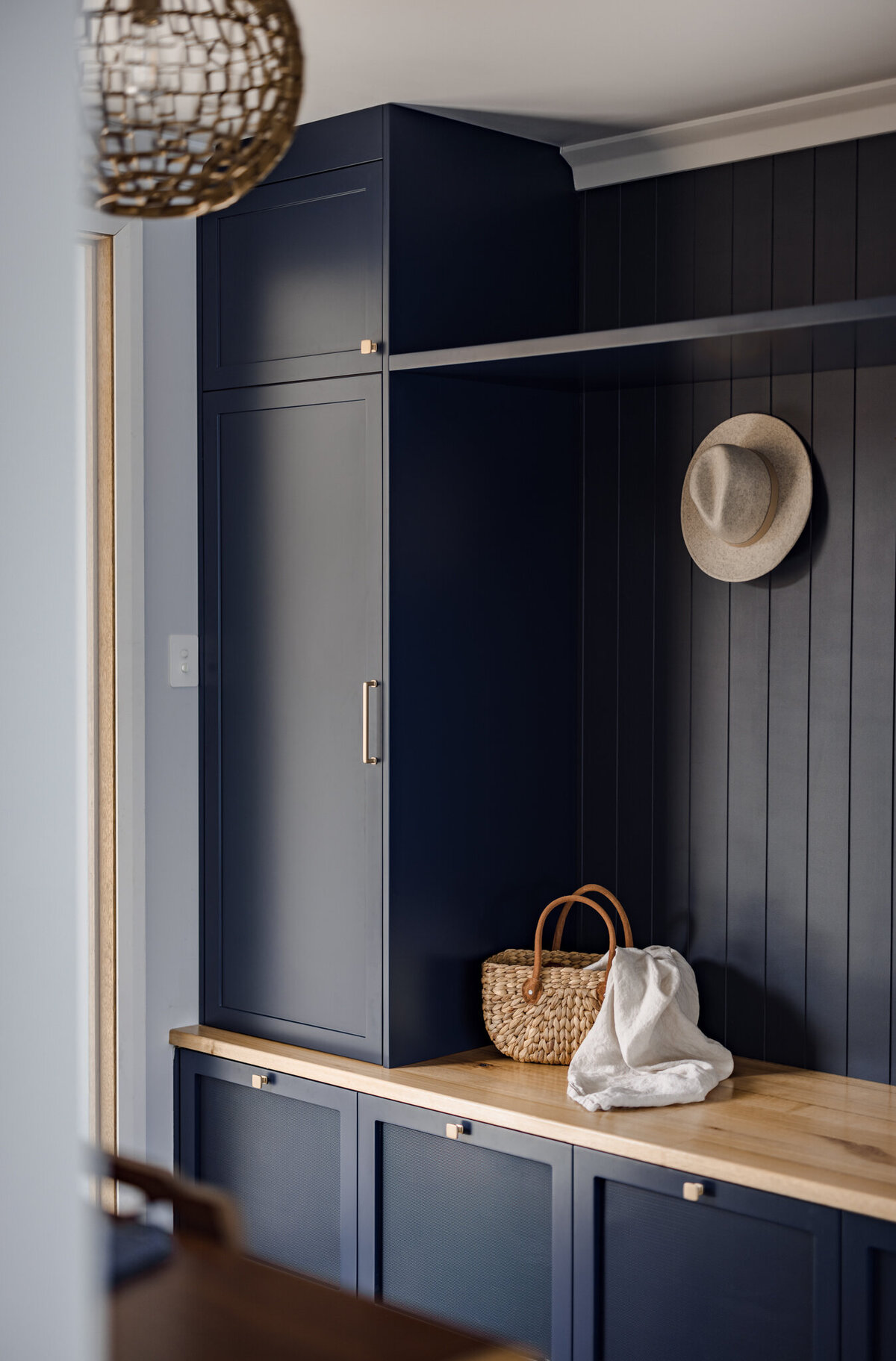 A woven basket, cloth, and straw hat rest elegantly on a wooden countertop in front of dark blue cabinetry, showcasing the sophisticated touch of a Newcastle Kitchen and Bathroom Designer.