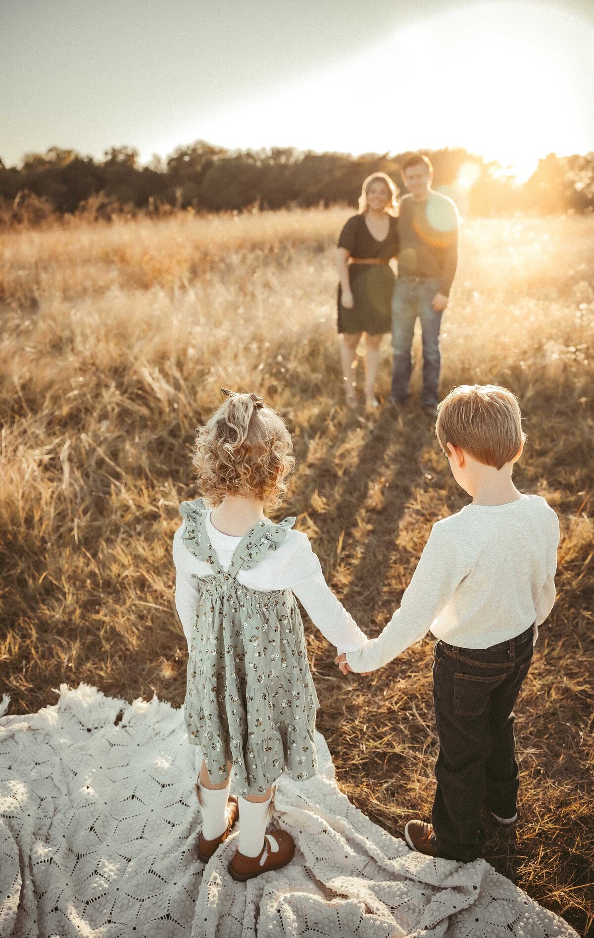 Girl and boy holding hands looking at their paernts who stand in the back of the photo with the texas sunset behind them