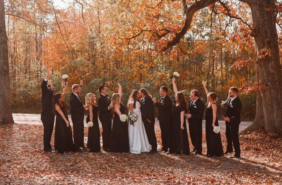bride and groom kissing while bridesmaids and groomsmen cheer them on with orange and yellow leaves around them