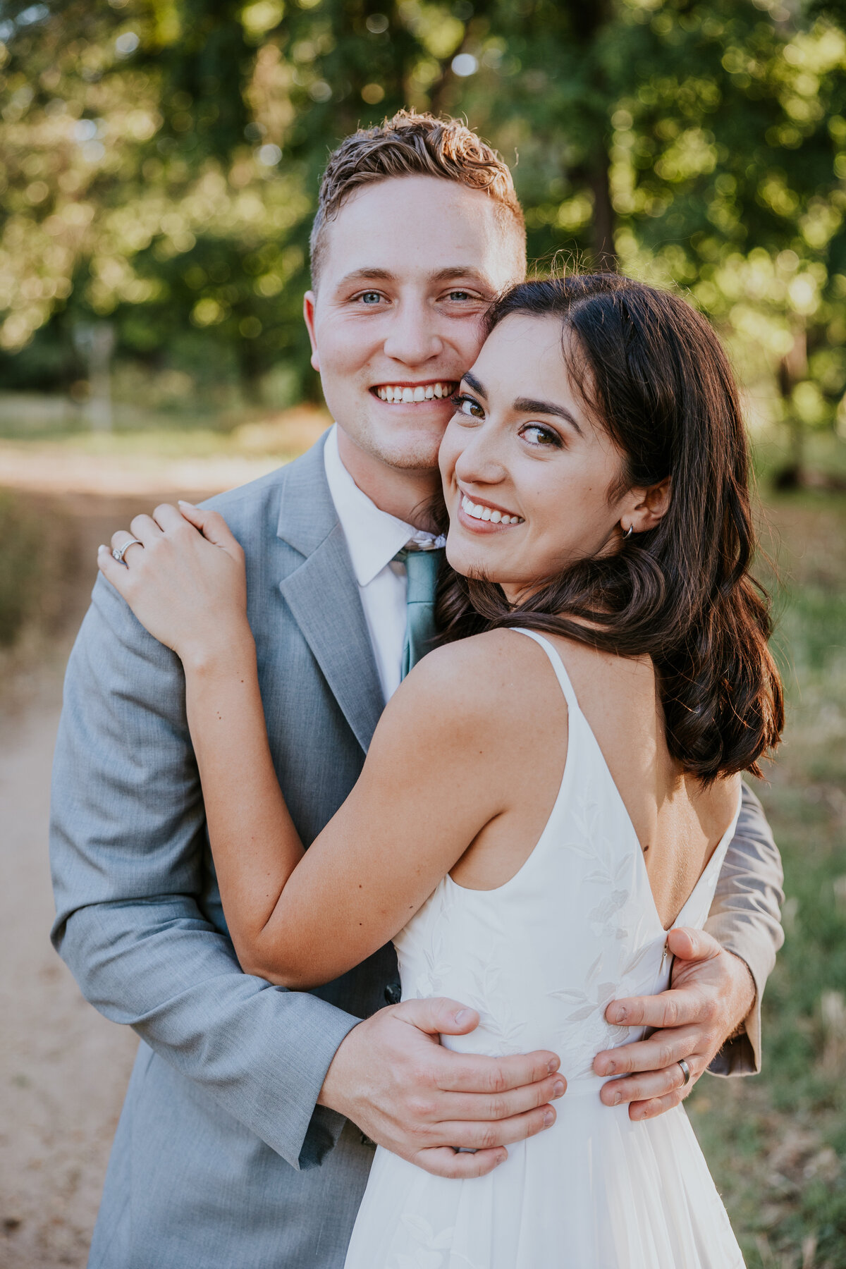 Bride places hand on grooms shoulder and both smile at camera.