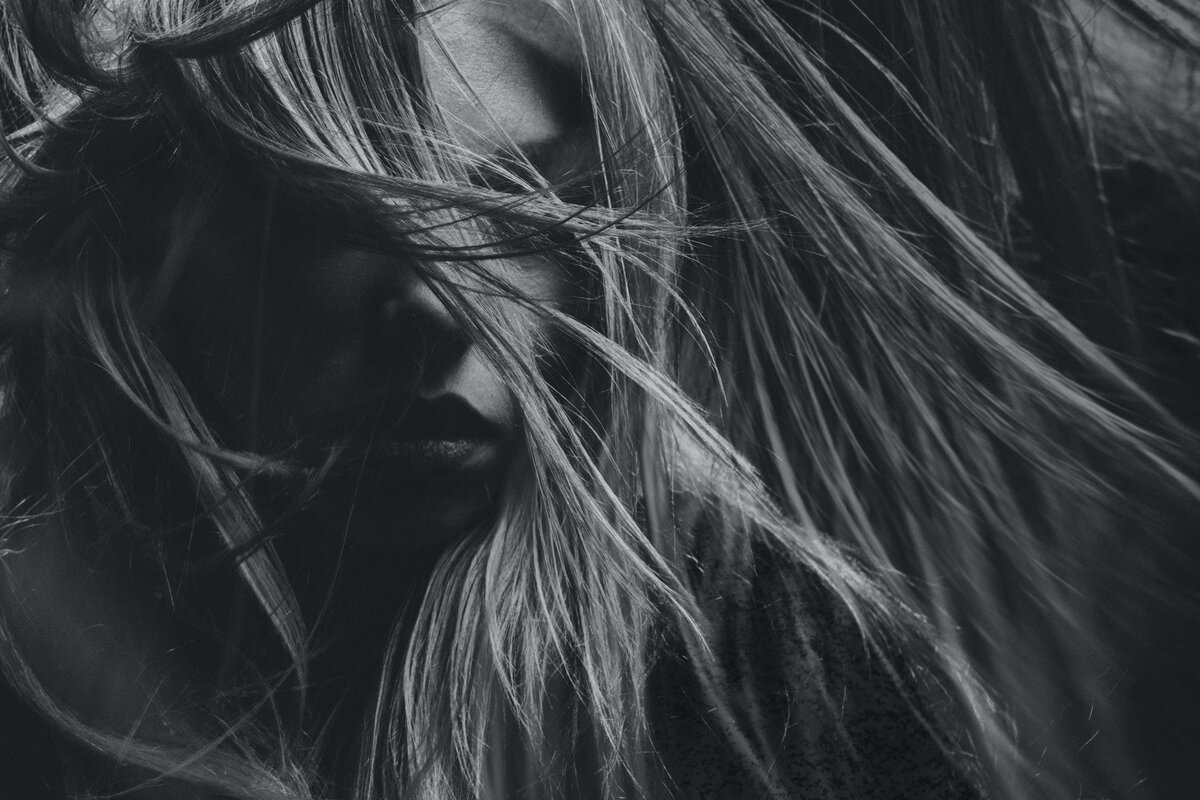 Close-up black and white photo of a person with long hair blowing across their face, partially obscuring their features, evoking the creativity found in logo and web design.