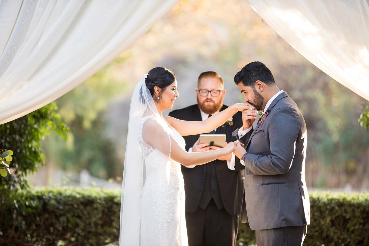 Groom kisses his Bride's hand as the officiant performs their wedding ceremony
