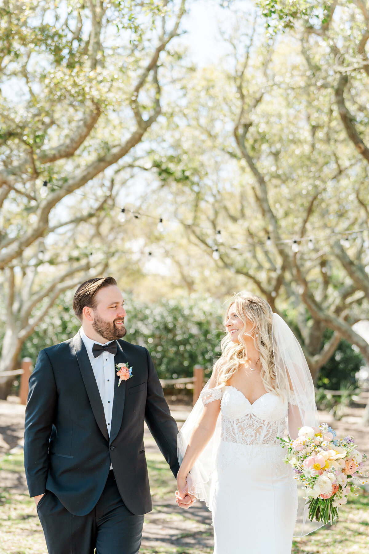 Newley weds walk through the beach trees holding hands 