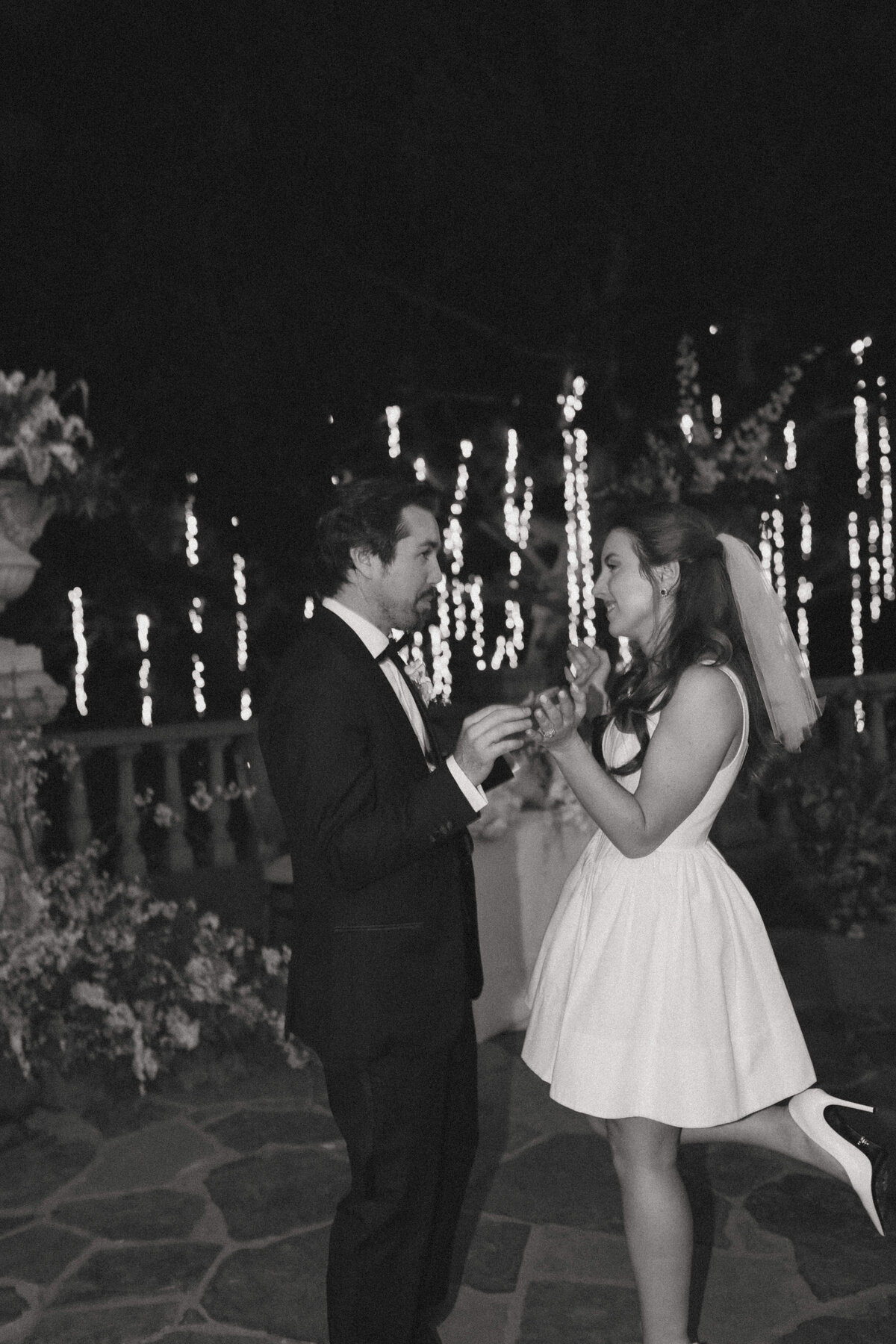 bride and groom dancing with each other during reception with big tree and hanging lights behind them