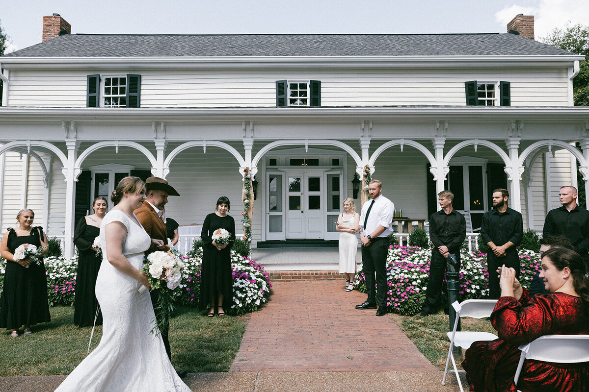 Bride and her father walk towards the groom on their wedding day, historic home featured in the background.