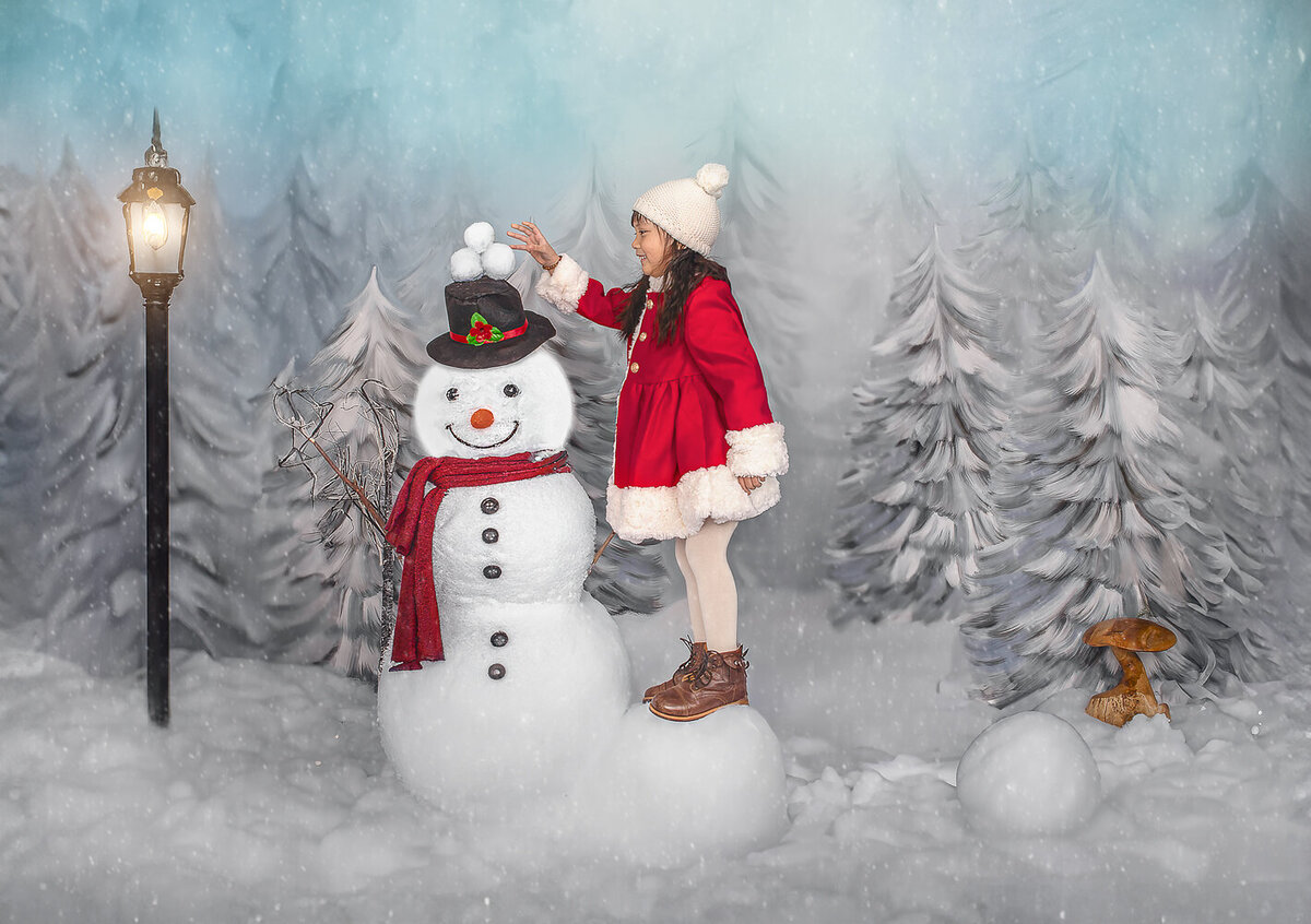 Young girl standing on a snowball and playing with a snowman in a winter wonderland themed studio session – Ottawa children’s photography by Sonia Gourlie