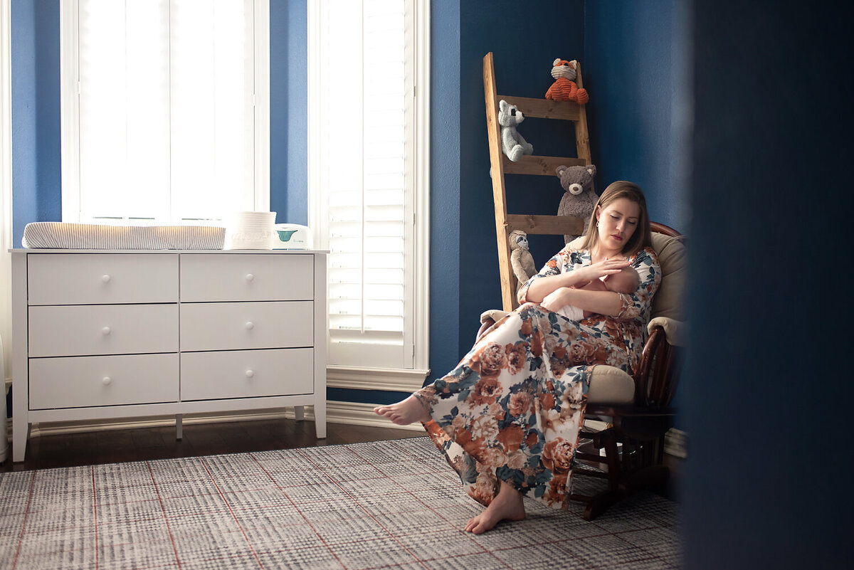 A mother sitting in a glider in her baby boy's blue nursery in Allen, TX