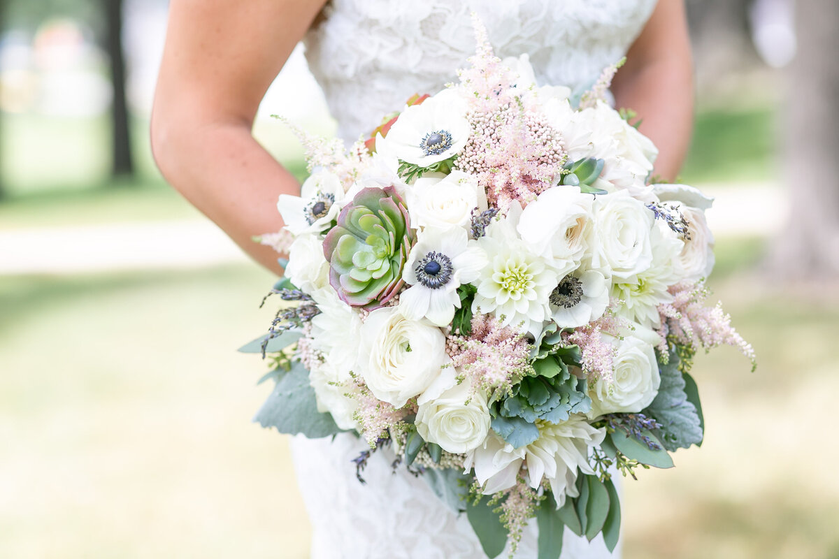 A white bride holding a large floral bouquet with white roses, anemones, astilbe, and succulents