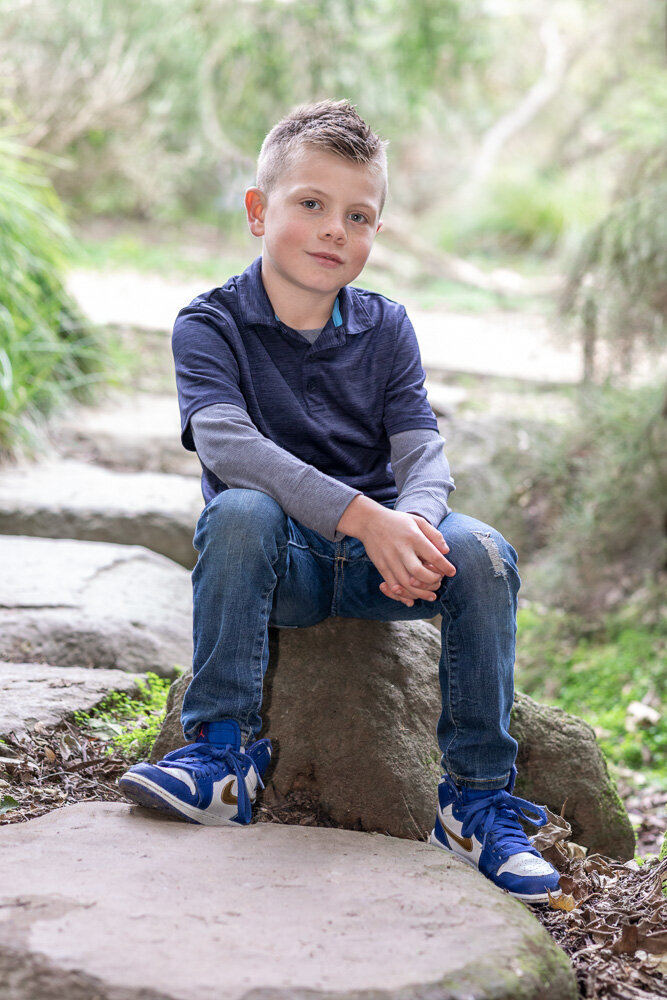 little boy sitting on rock outdoors