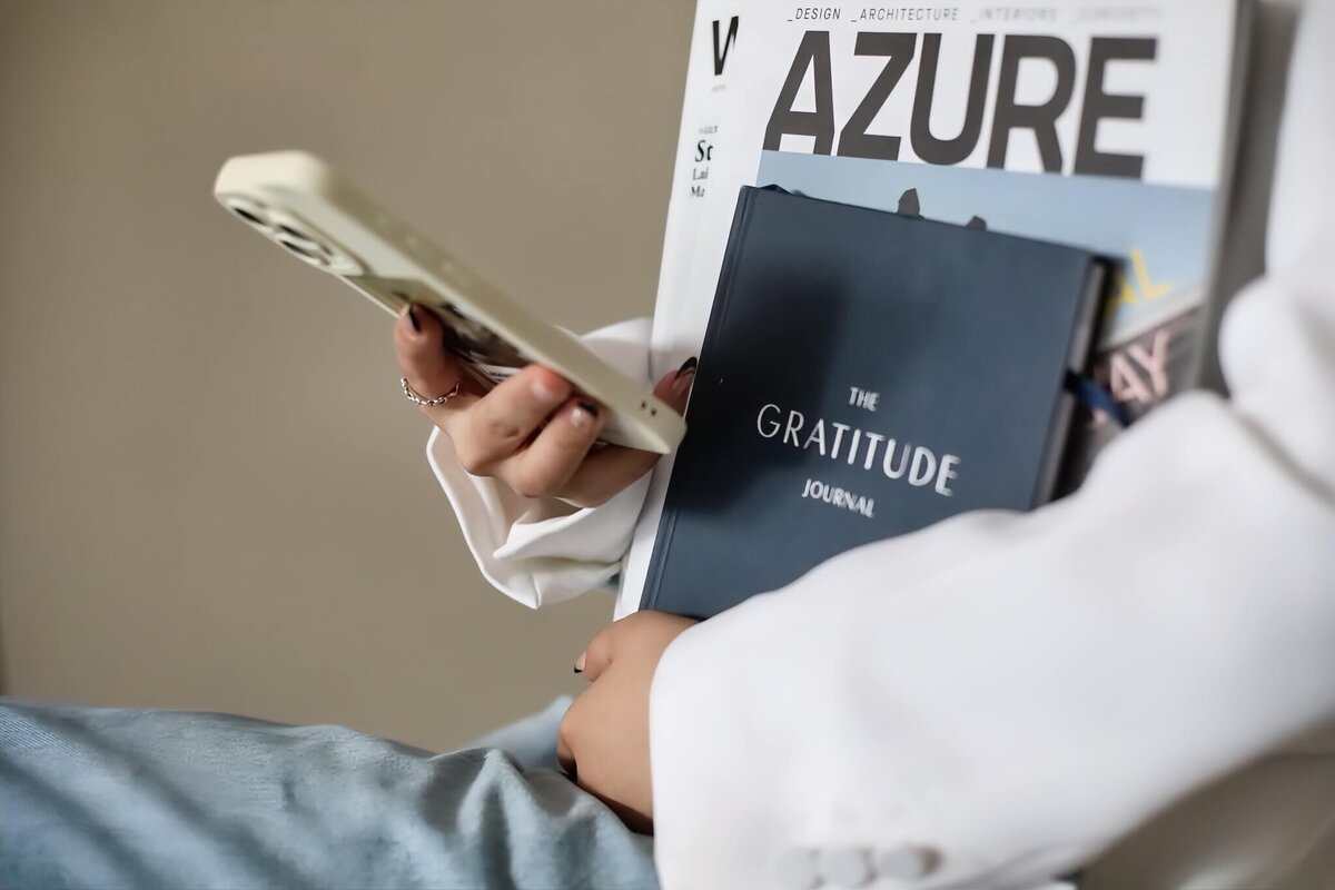 Close-up of a person holding a Gratitude Journal, an Azure magazine, and a smartphone, symbolizing mindfulness and productivity.