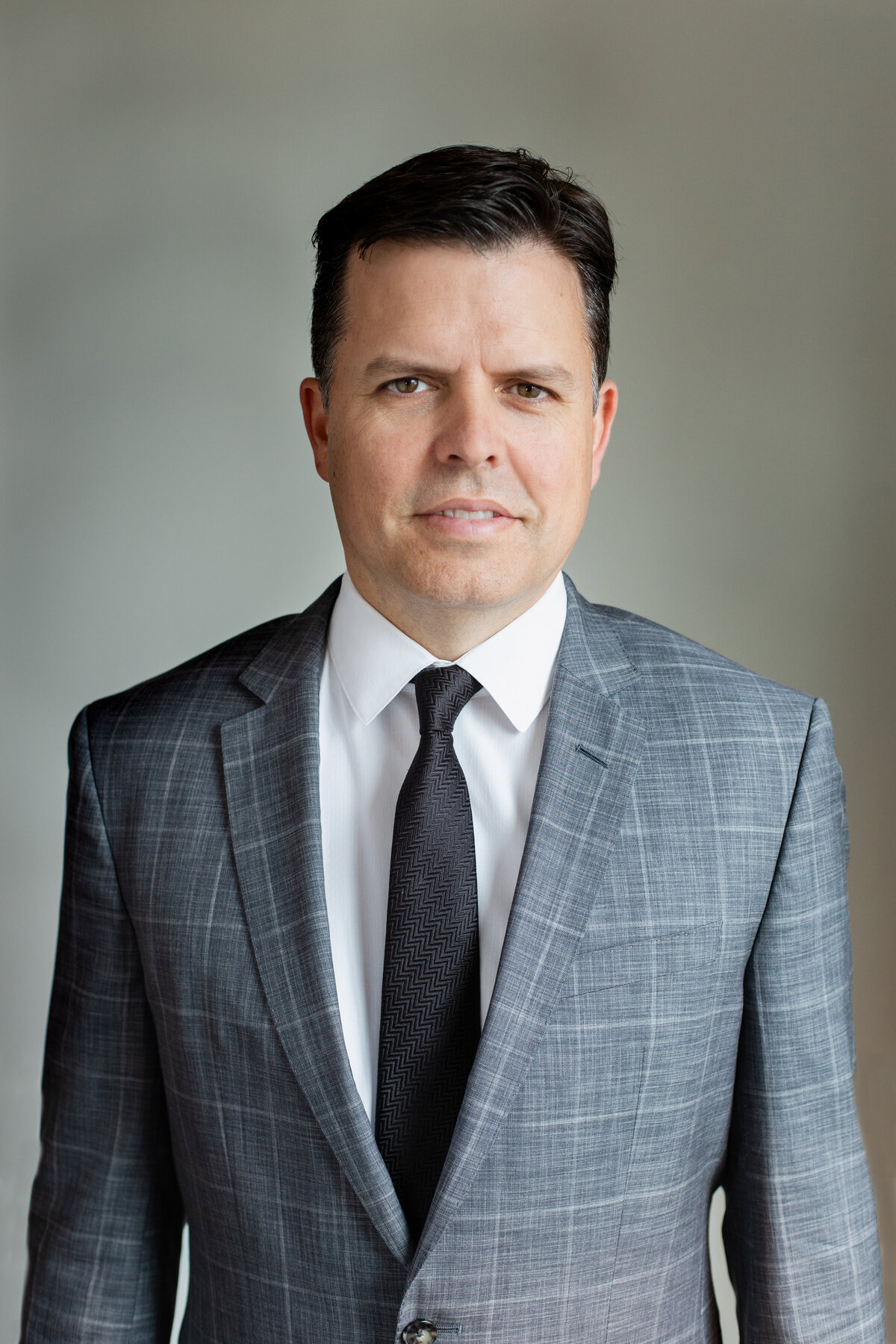 man in formal business grey suit and black tie standing in front of a grey wall