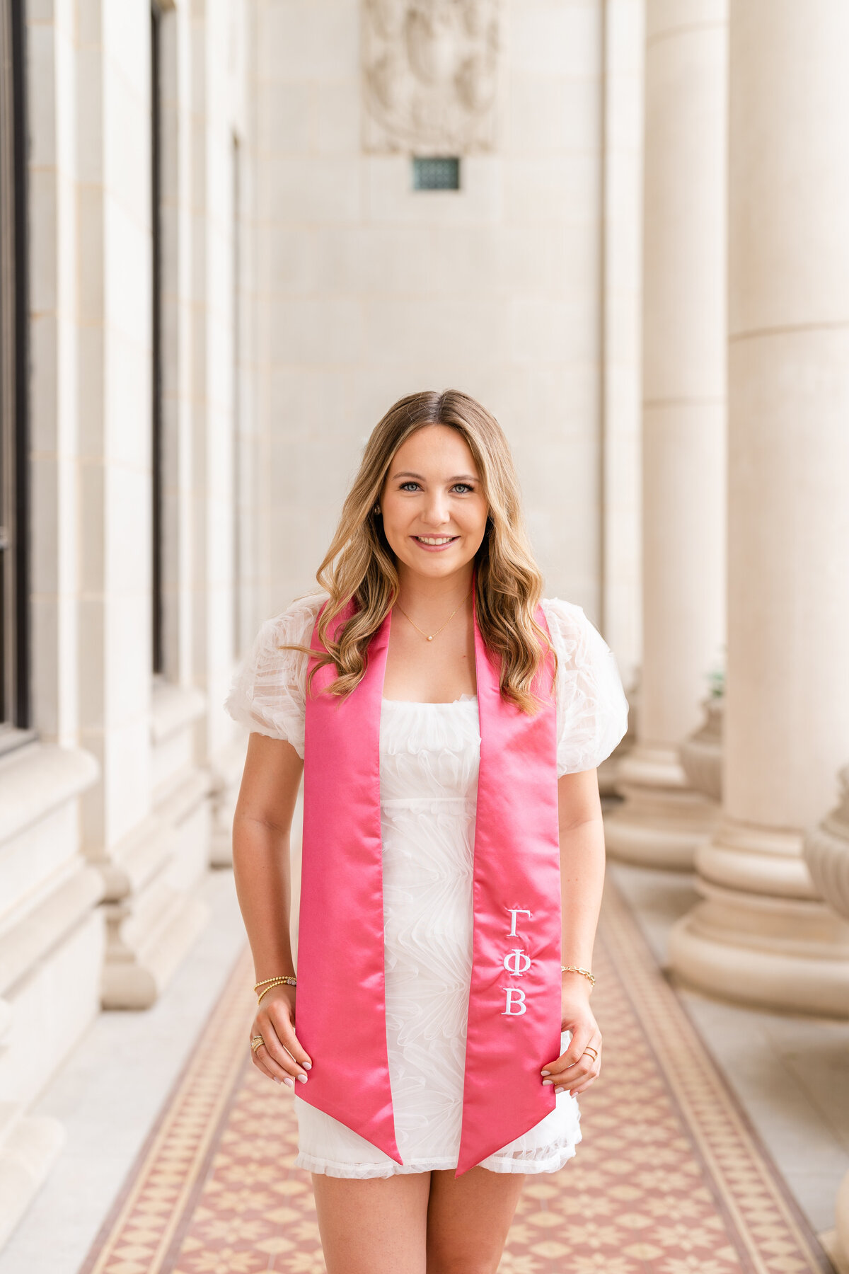 Texas A&M senior girl wearing Gamma Phi Beta stole and smiling with white dress in middle of Administration Building columns